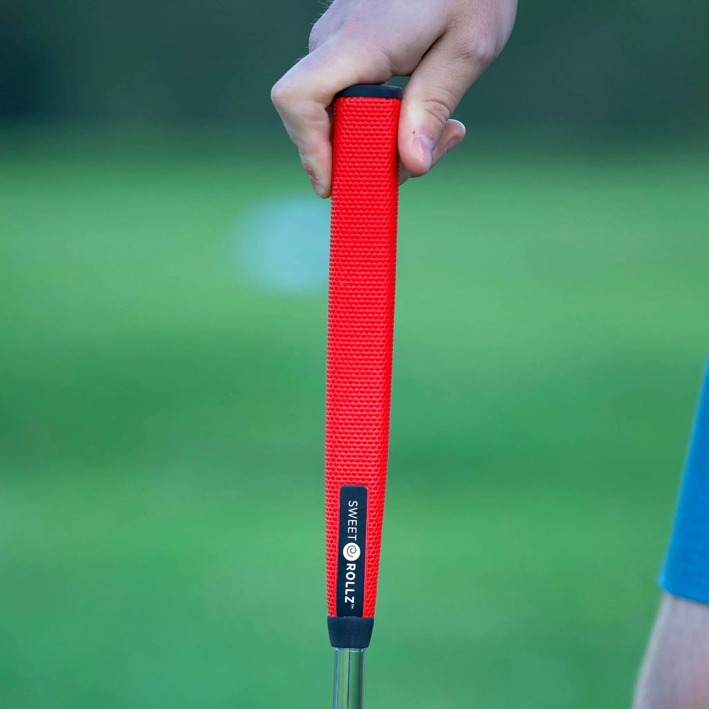 Sunday Red Midsize grip on putter, golfer's hand holding it with green background